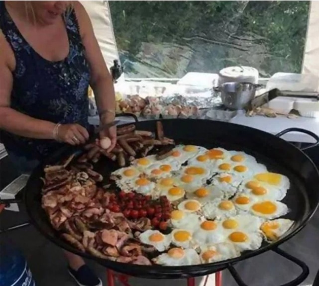 женщина разбивает яйцо на большую сковороду с едой
