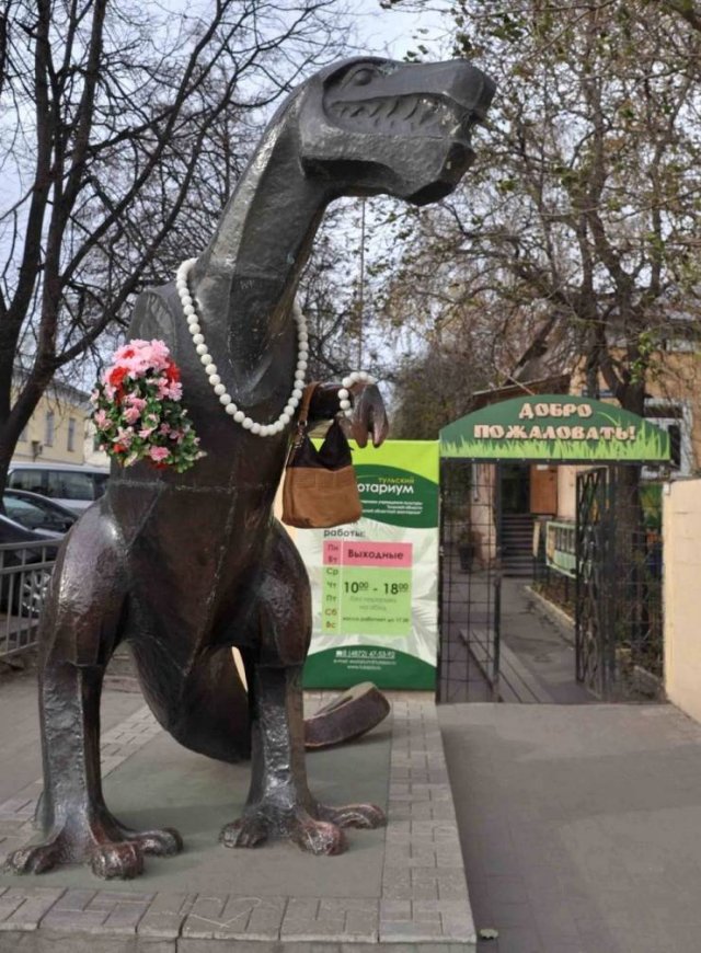 статуя динозавра с бусами и цветами